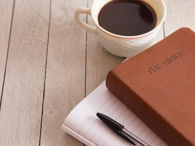 Bible on a desk with a notebook and a cup of coffee