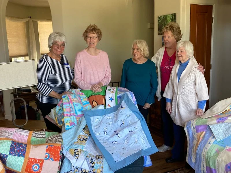 Nifty Needles members pose in front of quilts they have made