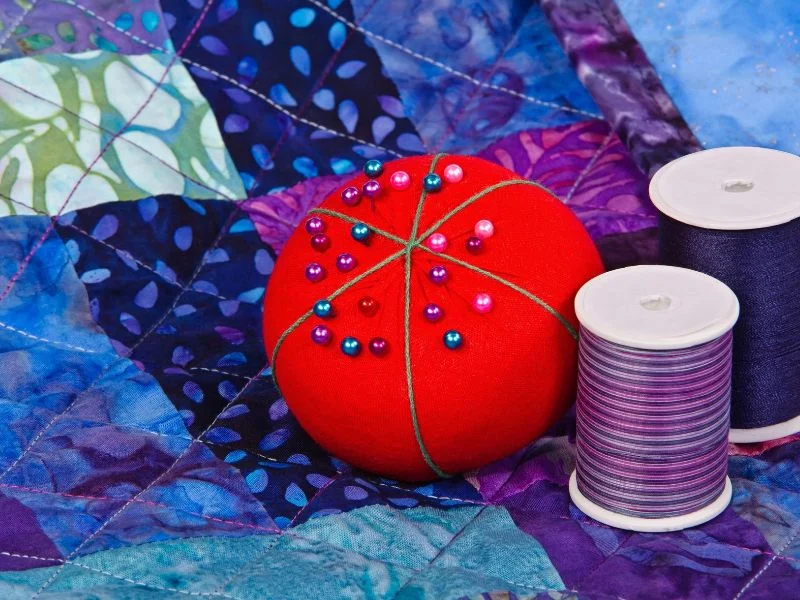 Pincushion and thread sitting on top of a purple and blue quilt